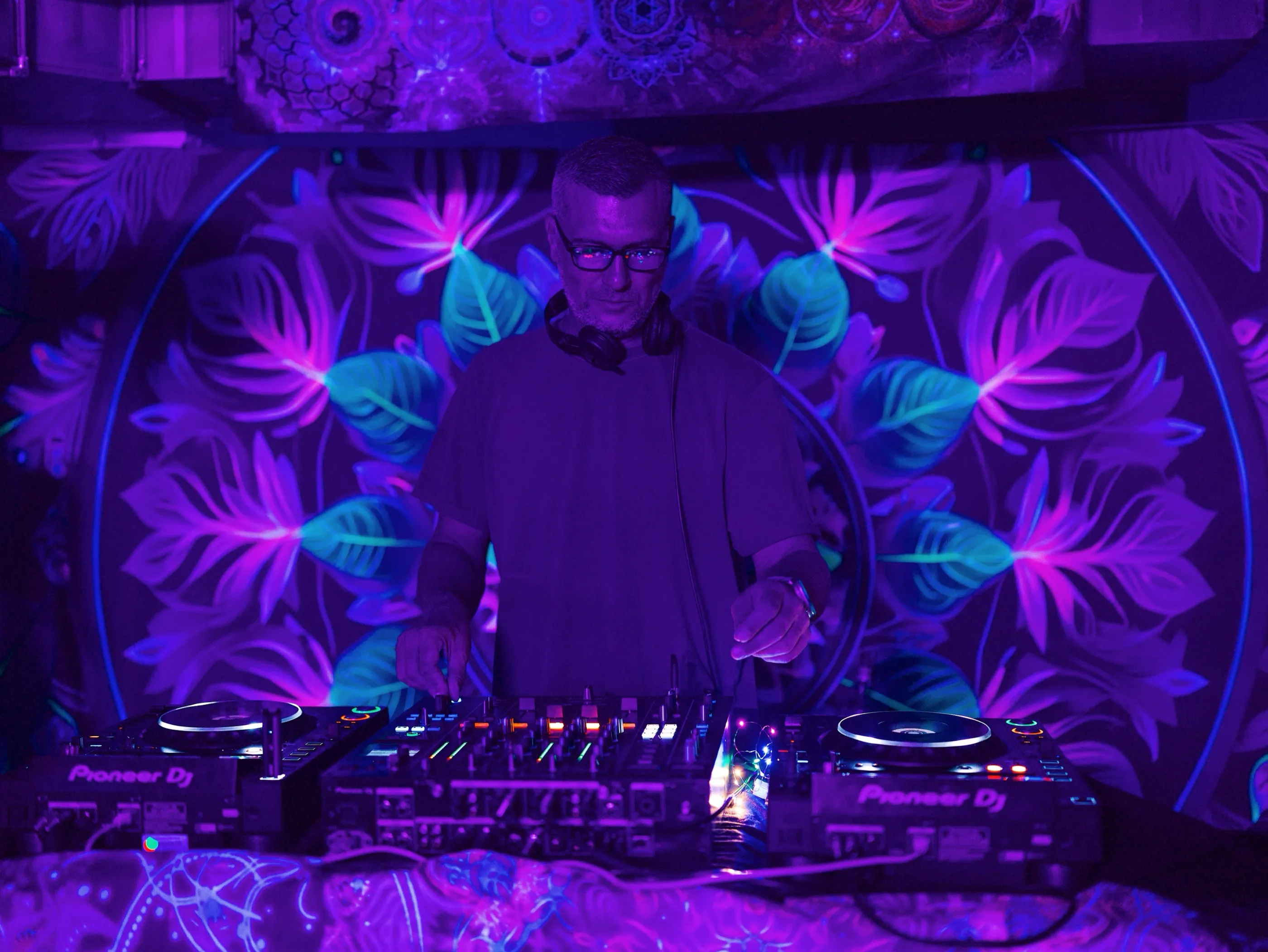 Ian Kita at the decks in front of a UV-lit floral backdrop